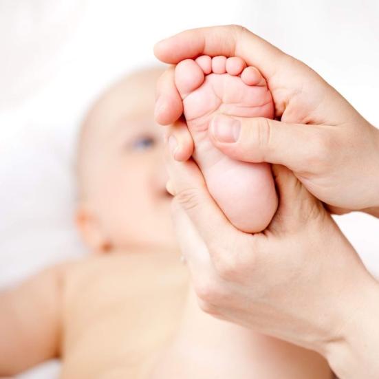 En baby ligger på ryggen med en fod i vejret. En voksen persons hænder masserer foden.