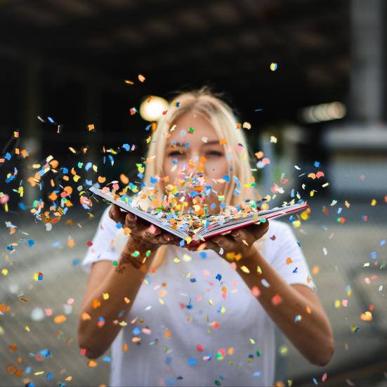 Ung kvinde der puster konfetti udover en bog