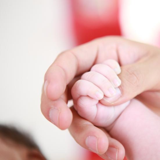 En babys hånd holder om tommelfingeren på en voksen persons hånd