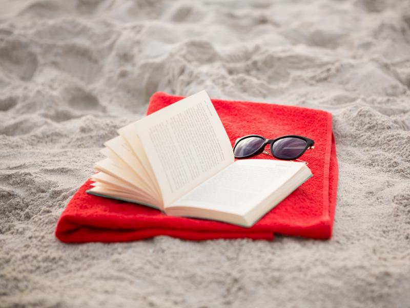 En bog, et håndklæde og solbriller ligger på stranden