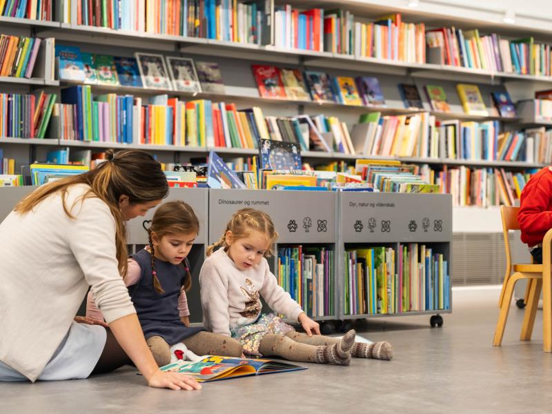 børn der sidder i biblioteksrummet og læser sammen med en voksen.jpg