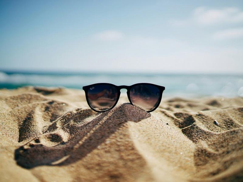 Billede af solbriller på sandstrand. Foto: Ethan Robertson, Unsplash.