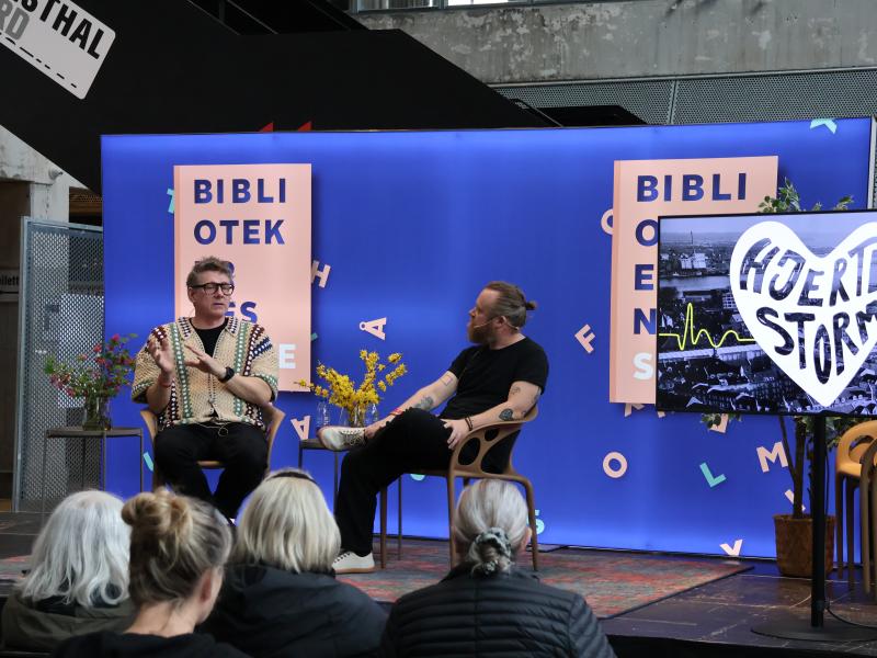 To mennesker, Jørgen (tv) og Teis (tv) sidder på en scene og taler foran et publikum