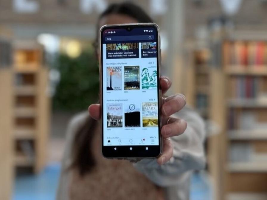 Line holder sin telefon frem til kameraet, telefonen viser app'en Biblioteket
