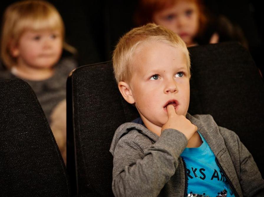 Børn sidder i biografsæder og kigger som om de kigger på en skærm.