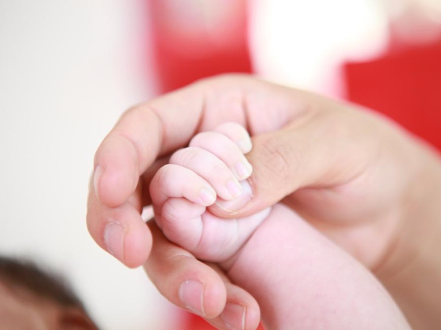 En babys hånd holder om tommelfingeren på en voksen persons hånd