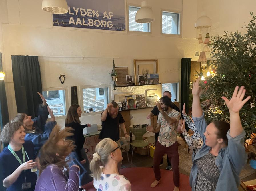 en gruppe mennesker danser i en rundkreds i Folkestuen på Hovedbiblioteket